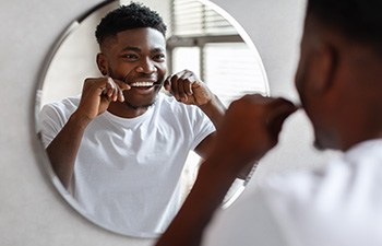 Man smiling while flossing in bathroom