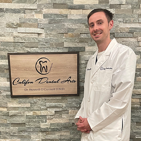 Doctor O Connell standing next to wooden sign for Califon Dental Arts