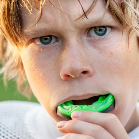 Young boy placing green athletic mouthguard over his teeth