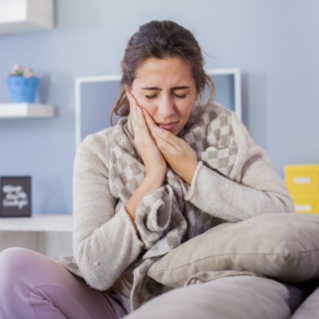 Woman on couch holding her cheek in pain