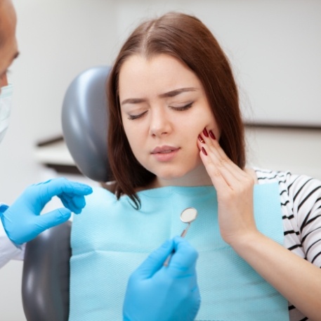 Woman holding her cheek in pain while visiting emergency dentist in Califon