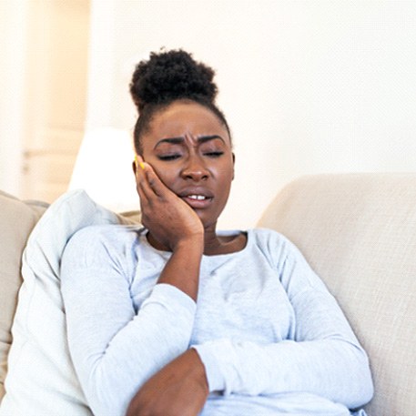 Woman experiencing toothache on couch at home