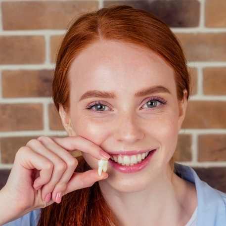 Smiling woman holding a tooth after tooth extraction in Califon