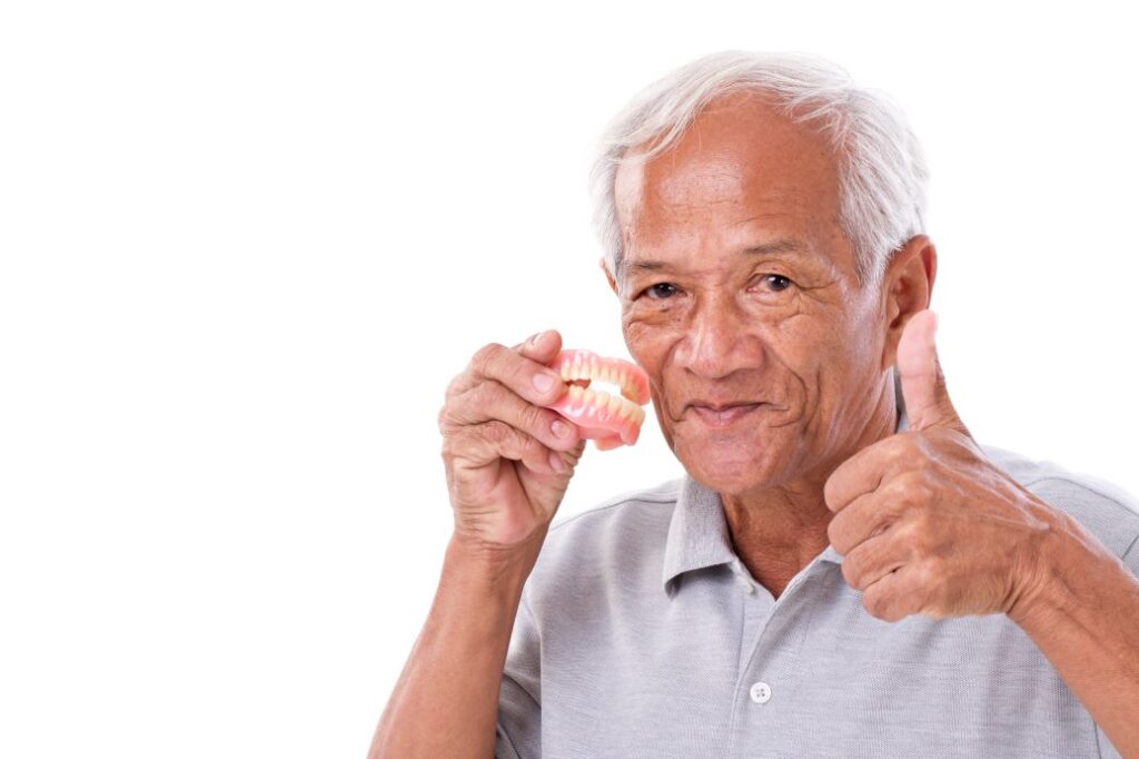 Smiling man holding dentures and giving the thumbs up sign.